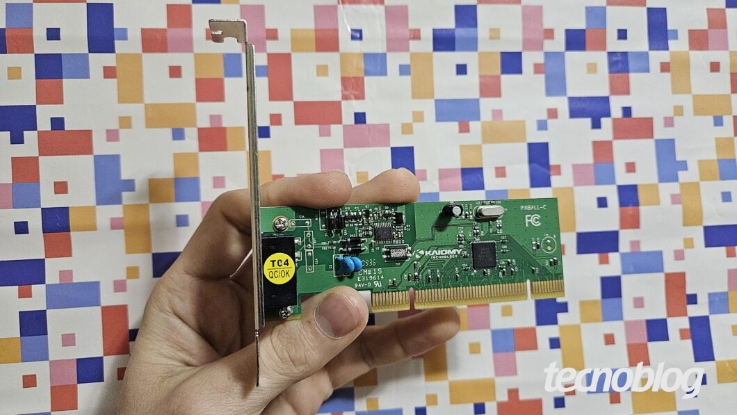 Mão segurando modem discado em formato de placa PCI sobre fundo abstrato