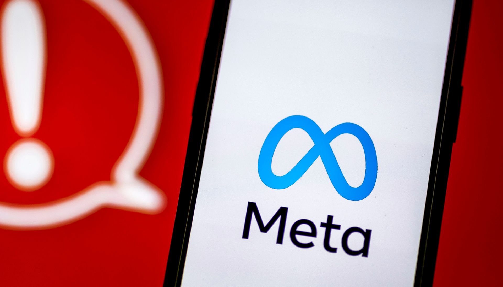 Um celular com a logo da Meta, atrás de um fundo com um sinal de aviso em vermelho.