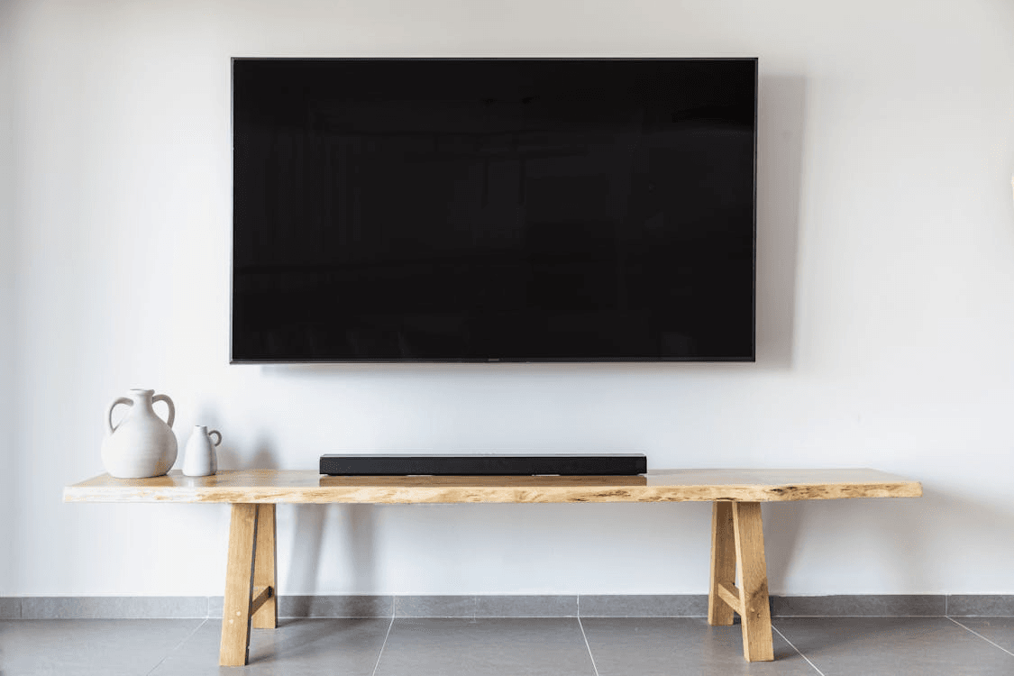 tv-grande-na-parede-com-soundbar-preta-em-bancada-de-madeira-decoracao-minimalista-sala-moderna